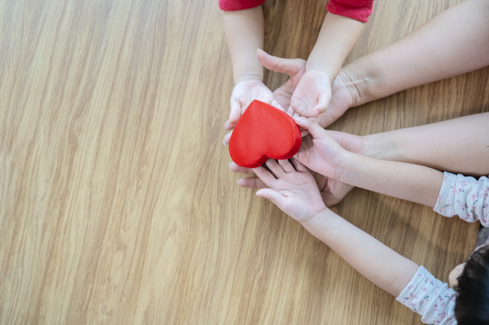 A child's and parent's hands holding a red heart together